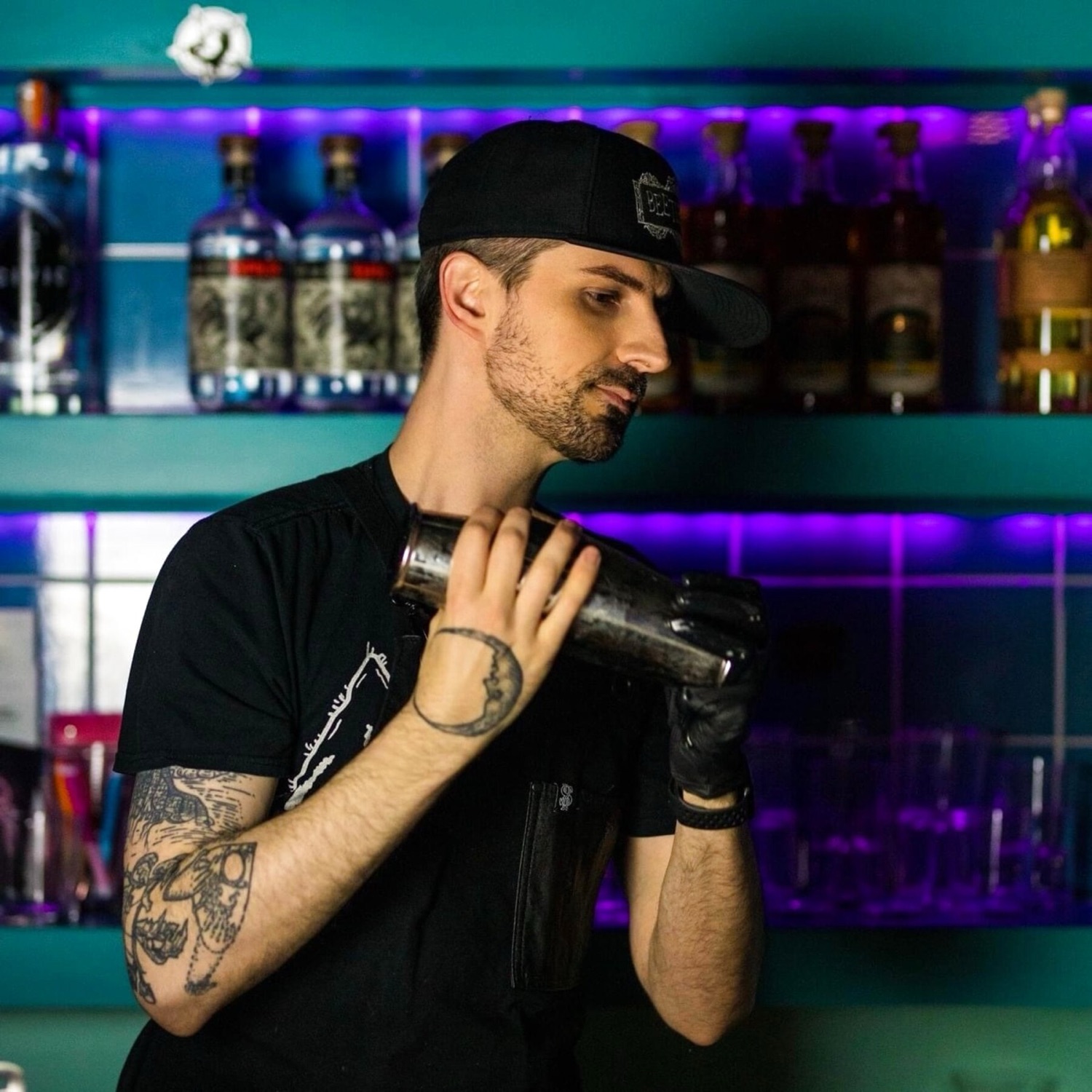 Kit shaking a cocktail in front of a lit back bar